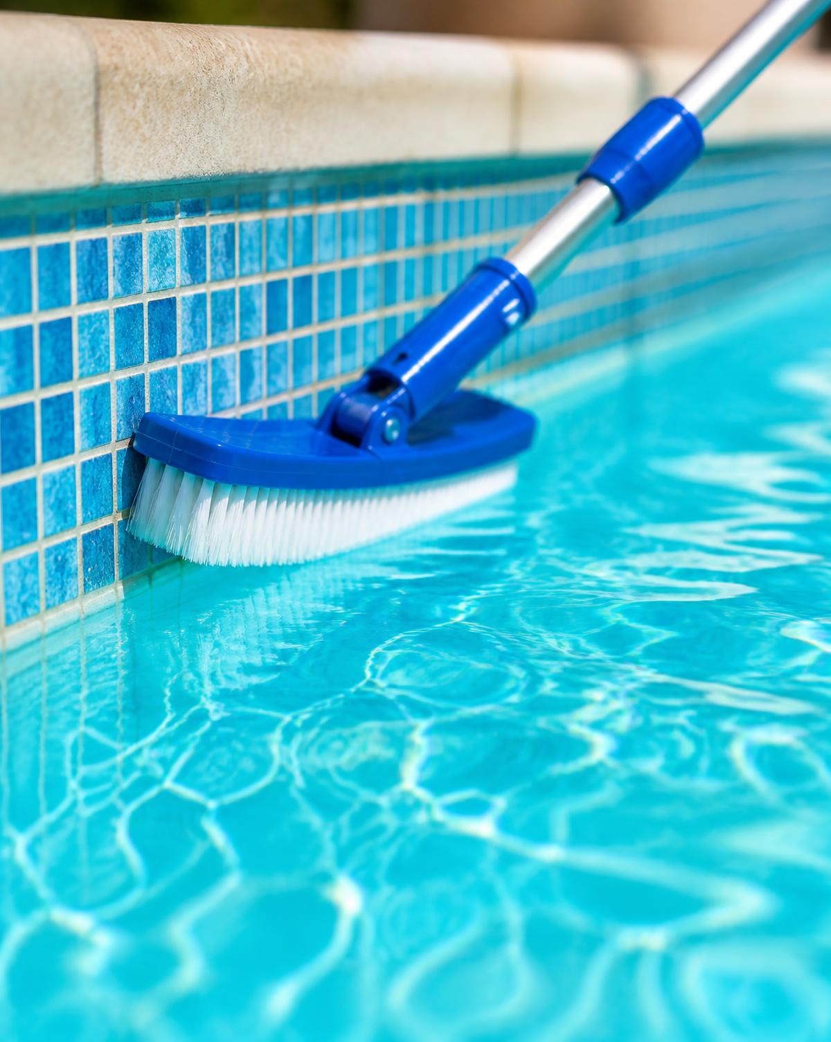 Pool cleaning brush sweeping along the waterline tile of a bright turquoise pool